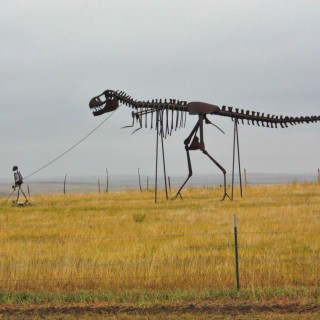 On the Road. Gassi gehen mal anders.... - Skulptur, Statue, Skulpturen, Figuren, Dino, Dinosaurier, Skelett, Tyrannosaurus rex, Midland, Stamford, Metallfiguren, T-Rex, Clarence Hullinger, Altmetall - (Stamford, Midland, South Dakota, Vereinigte Staaten)