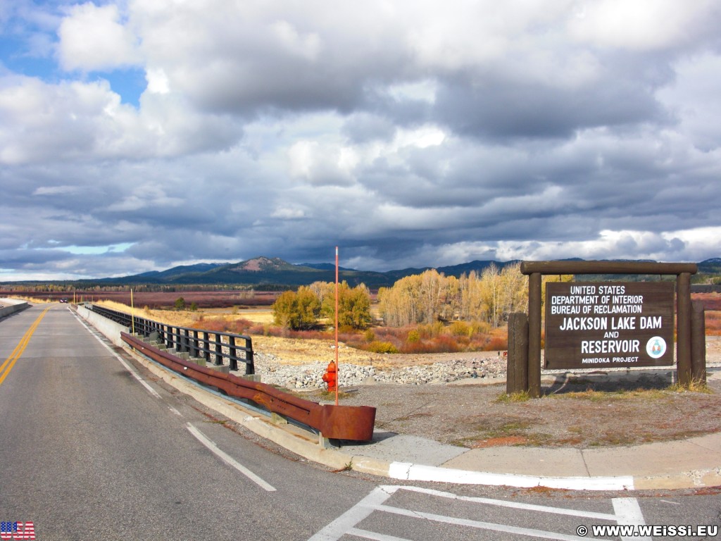 Grand-Teton-Nationalpark. Jackson Lake Dam und Reservoir. - Wolken, Schild, Landschaft, Tafel, Ankünder, Bäume, Geländer, Jackson Lake Dam, Jackson Lake Reservoir, Staudamm - (Colter Bay Village, Moran, Wyoming, Vereinigte Staaten)