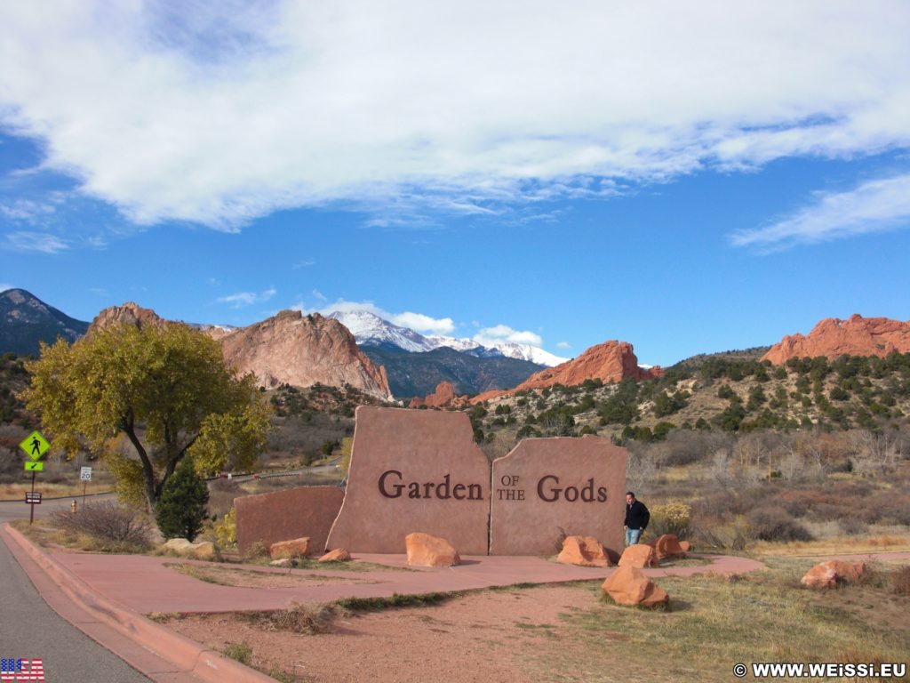 Garden of the Gods. Schild am Haupteingang des Parks. Im Hintergrund sieht man den mit Schnee bedeckten Gipfel des Pikes Peak. - Sehenswürdigkeit, Landschaft, Panorama, Aussichtspunkt, Park, Felsformationen, Garten der Götter, Naturpark, sehenswert, Kindergarten Rock, North Gateway Rock, Pikes Peak, South Gateway Rock - (Glen Eyrie, Colorado Springs, Colorado, Vereinigte Staaten)