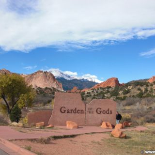 Garden of the Gods. Schild am Haupteingang des Parks. Im Hintergrund sieht man den mit Schnee bedeckten Gipfel des Pikes Peak. - Sehenswürdigkeit, Landschaft, Panorama, Aussichtspunkt, Park, Felsformationen, Garten der Götter, Naturpark, sehenswert, Kindergarten Rock, North Gateway Rock, Pikes Peak, South Gateway Rock - (Glen Eyrie, Colorado Springs, Colorado, Vereinigte Staaten)